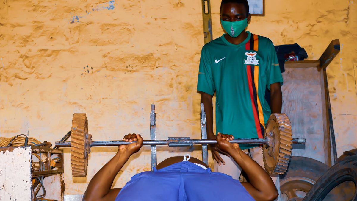 Man performing a bench press in a local gym with a training partner nearby